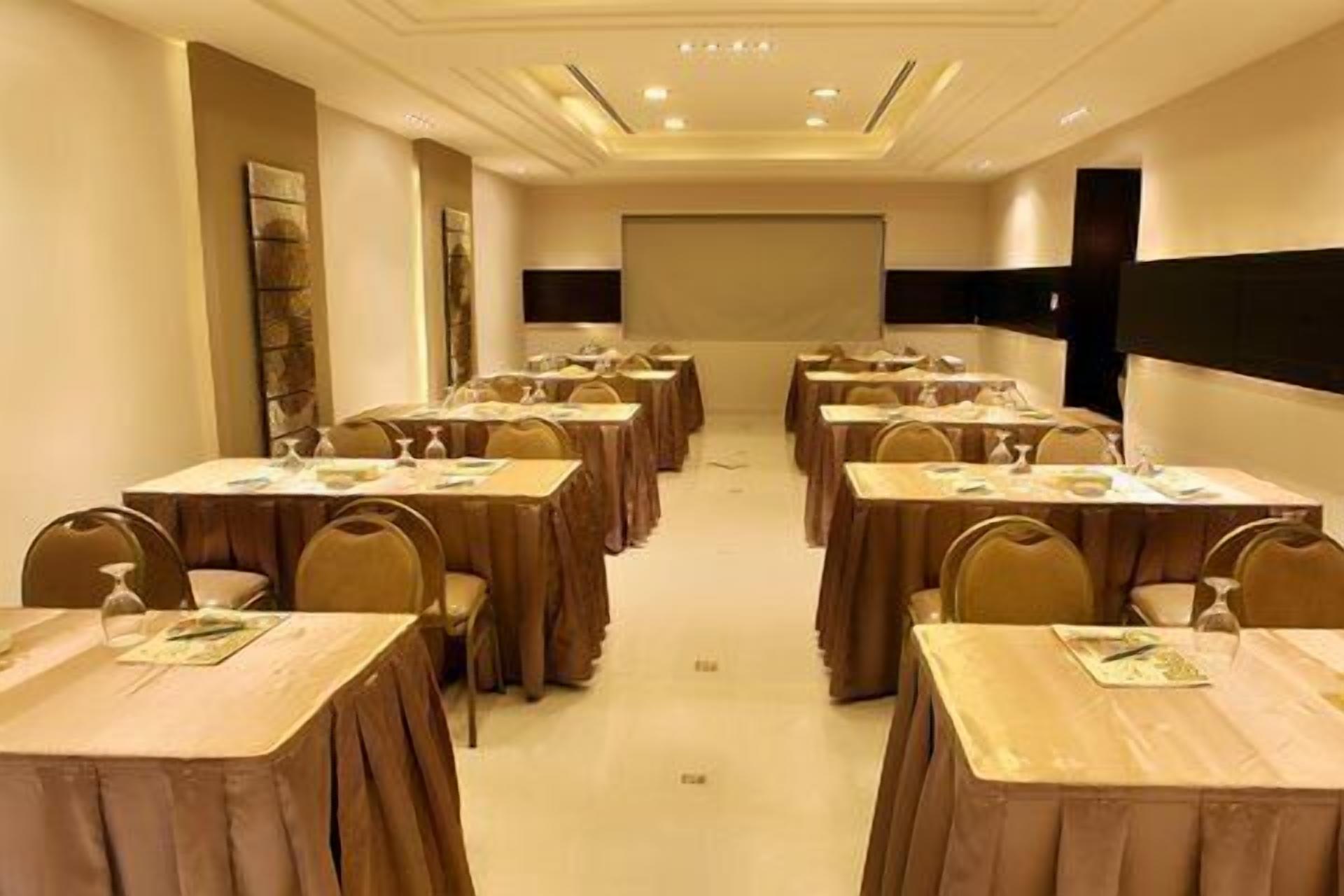 Une salle de conférence dotée de plusieurs tables et chaises, d’un écran de projection à l’avant et d’une décoration aux couleurs neutres.