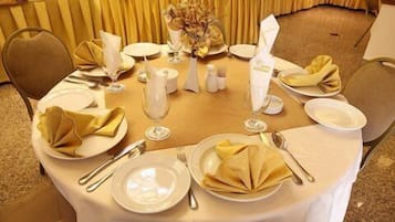 A round dining table set with white plates, gold napkins, and silverware, surrounded by chairs.