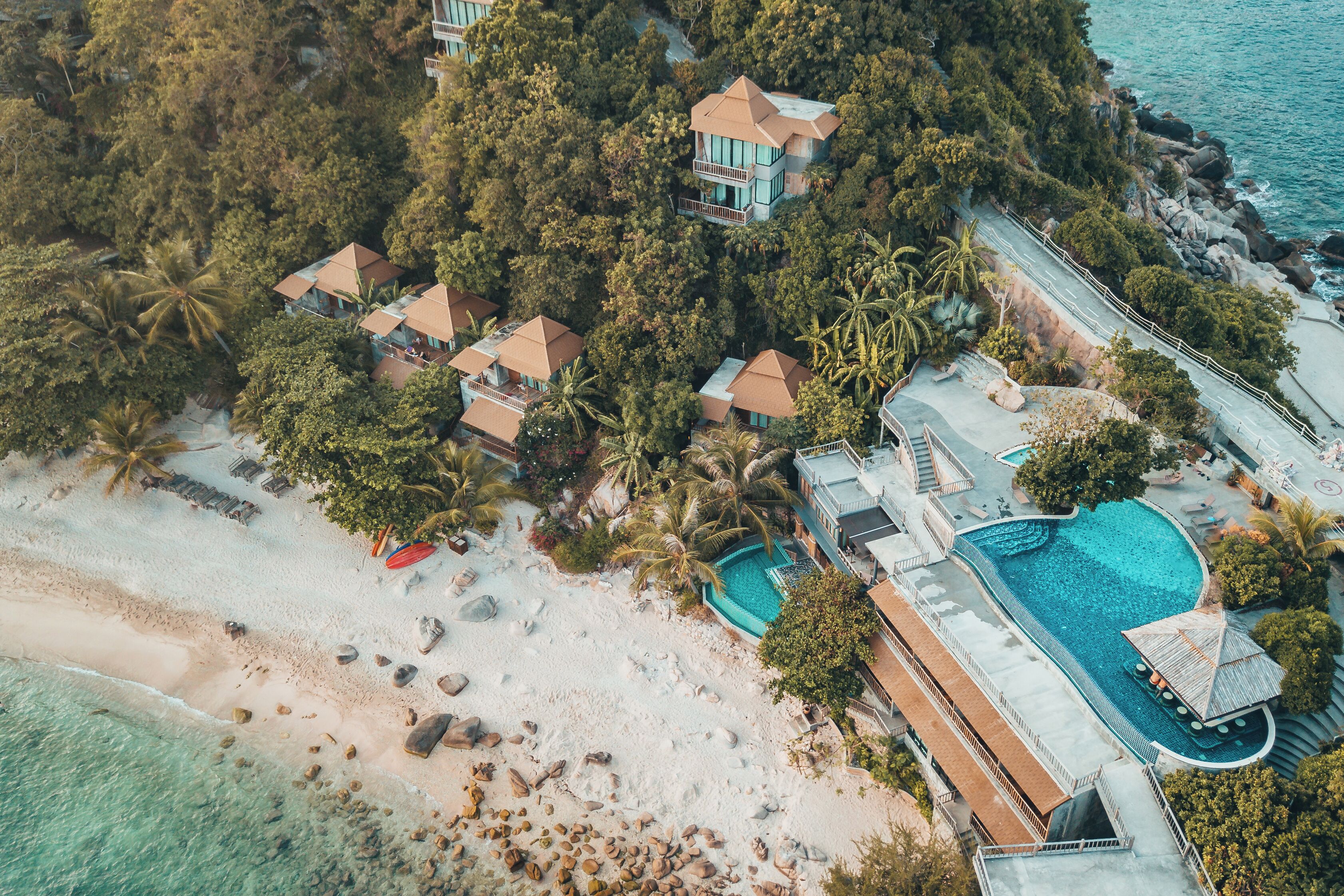 Vista aérea de una propiedad costera con varias villas, una playa y una piscina.