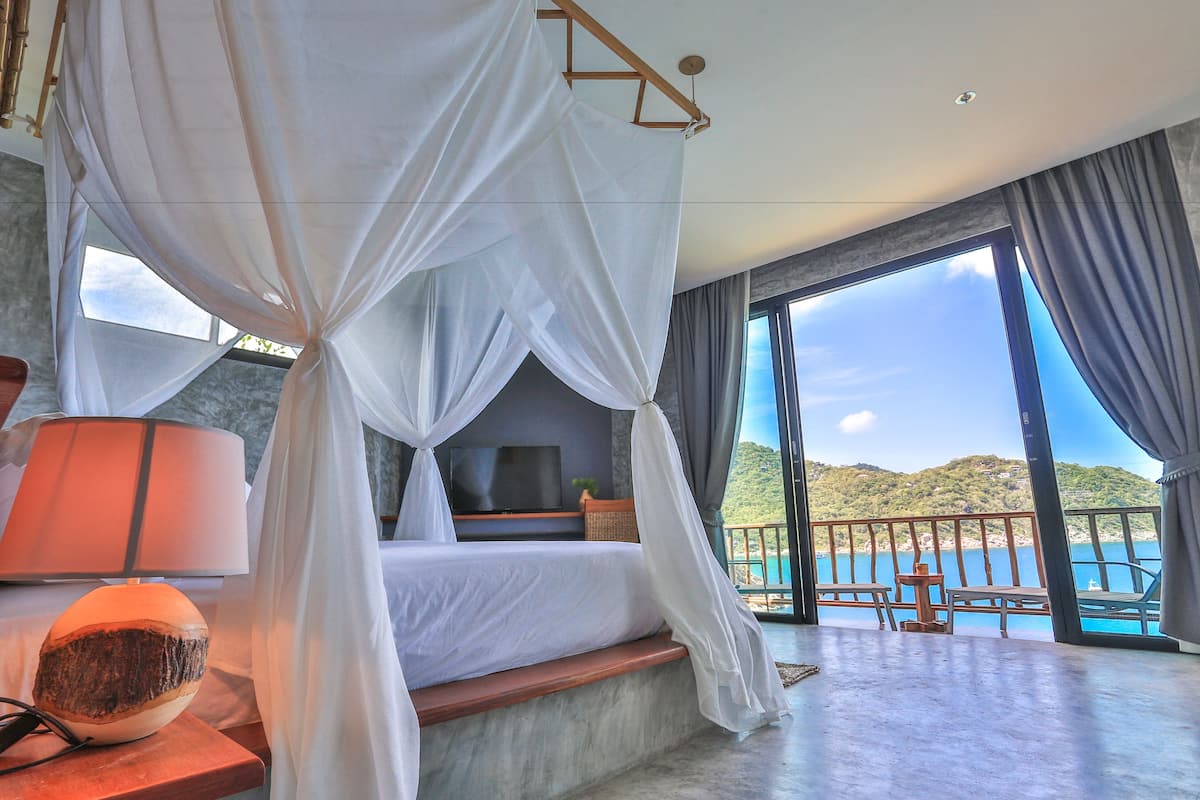 A bedroom with a bed, a TV, a bedside lamp, and a view of the sea.