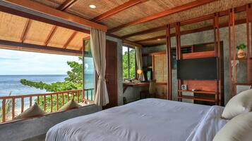 A bedroom with a large bed, a desk with a computer, a TV, and a view of the ocean.
