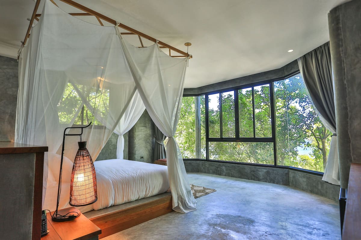 A bedroom with a canopy bed, large windows, and a bedside lamp.