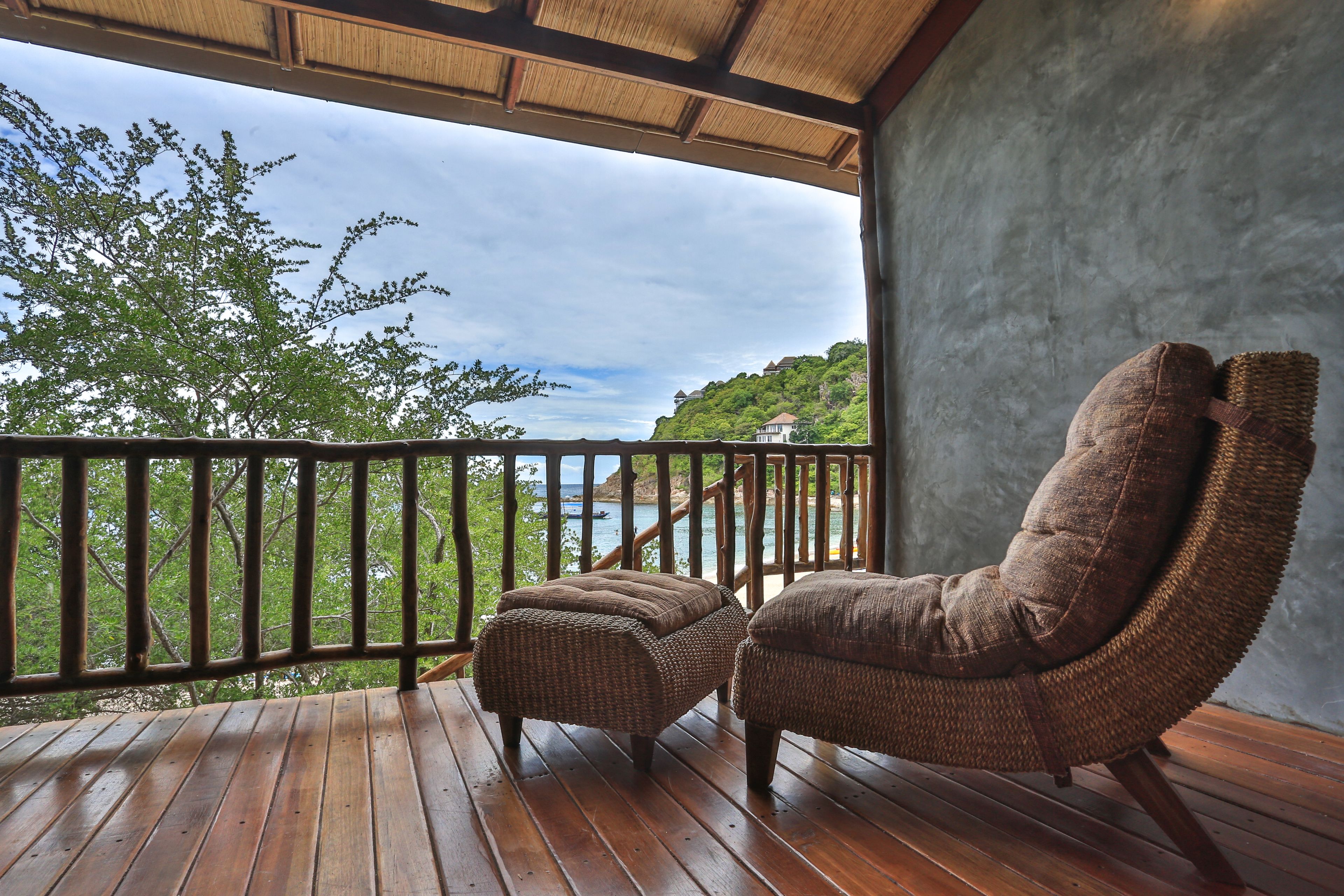 A wooden deck with wicker furniture overlooking a scenic view of a coastline.