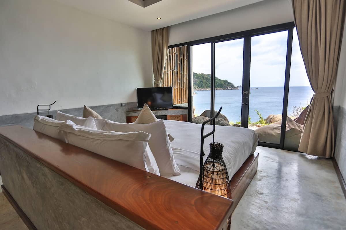 A bedroom with a large bed, a TV, and a view of the sea.
