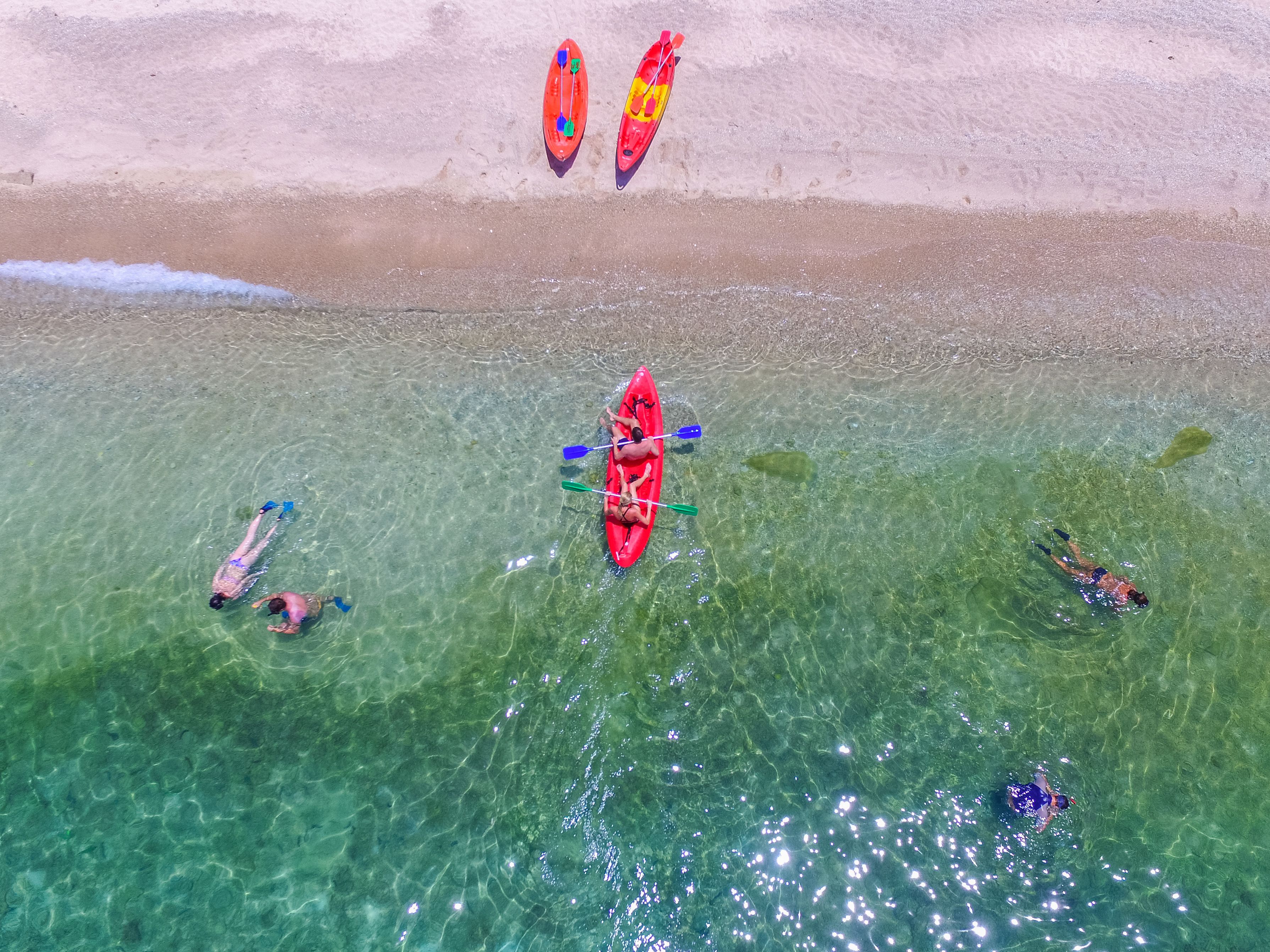 A beach with kayaks and people in the water.
