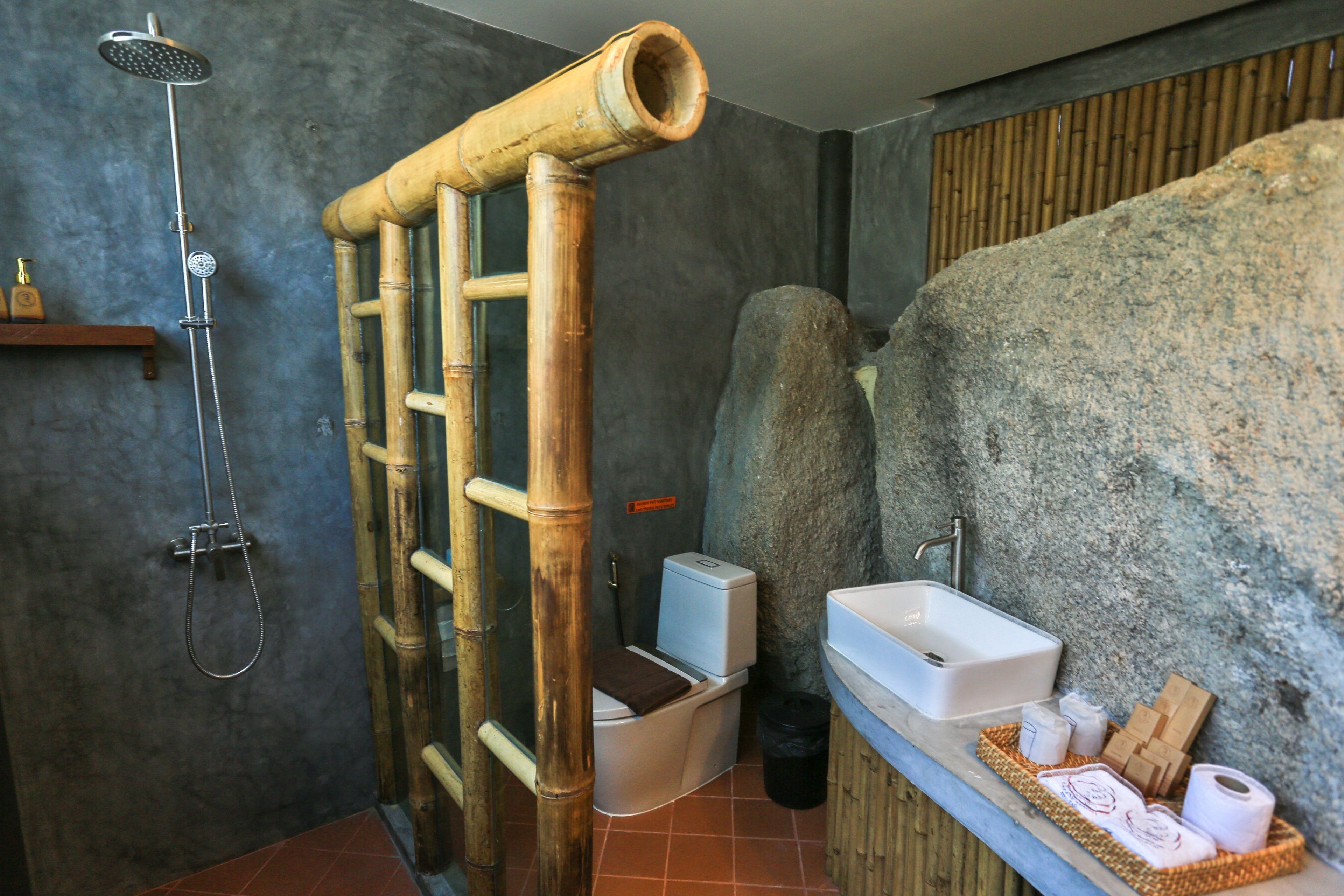 A bathroom with a bamboo shower, a toilet, and a sink with toiletries.