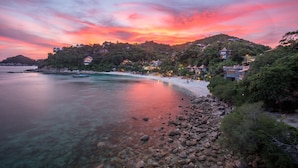 A coastal area with clear waters, rocky shoreline, and buildings on a hillside. - Sai Daeng Resort (Koh Tao)