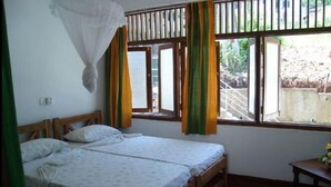 A room with two wooden beds, a mosquito net, and a window with curtains. - Hotel Mango Garden (Kandy)