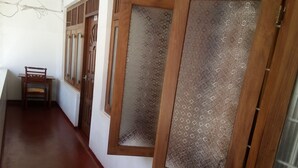 A corridor with wooden doors and windows, a wooden chair, and a tiled floor. - Hotel Mango Garden (Kandy)