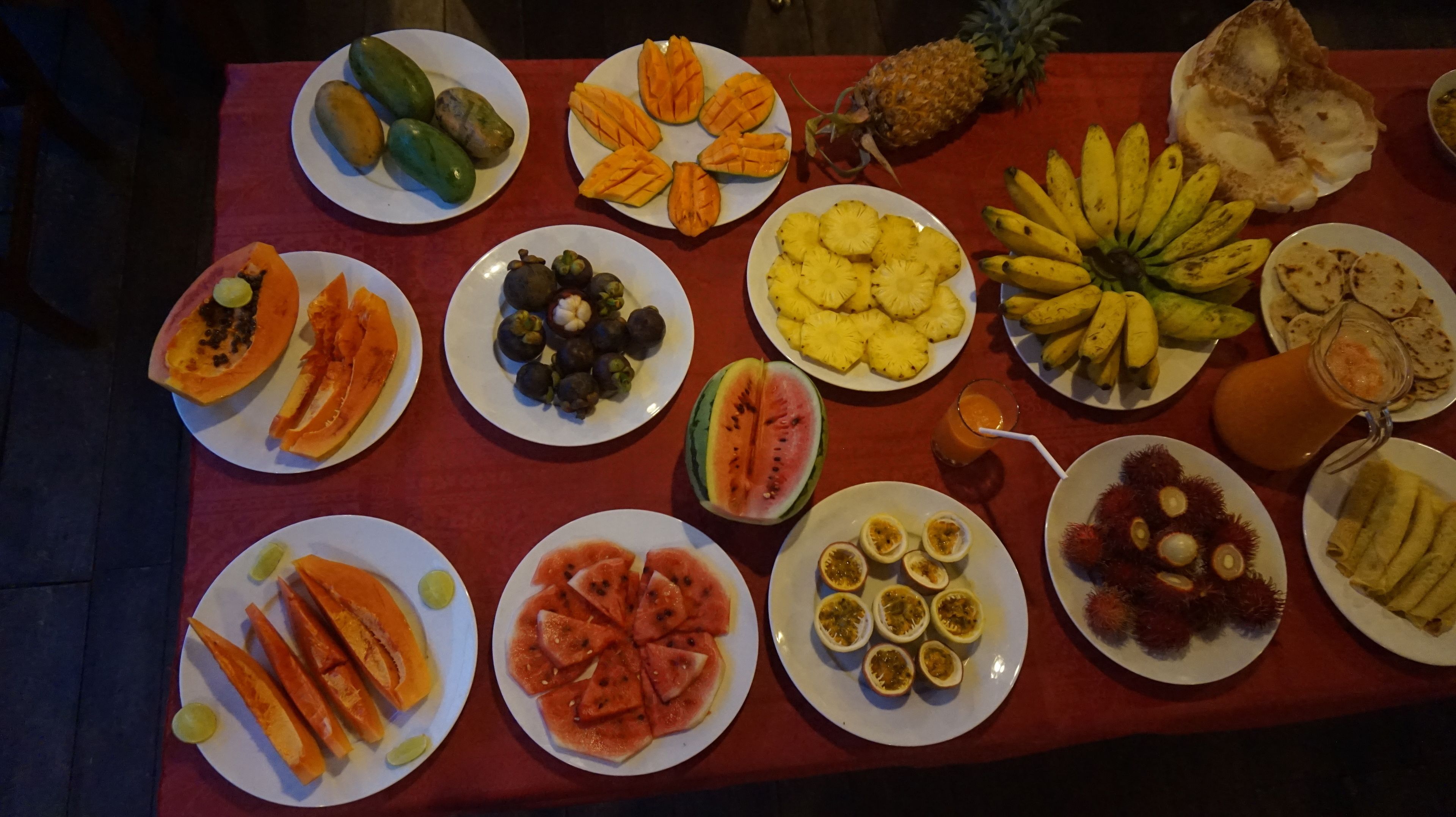 A table with various fruit plates, including mangoes, pineapples, bananas, papayas, and watermelons.