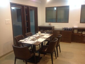 A dining area with a rectangular table set for six, surrounded by six chairs. There is a kitchen area with a countertop and cabinets to the right.
