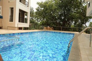 A swimming pool with a metal ladder, surrounded by a tiled deck and a railing. - La Vida Studio Inn Baga - Goa By Lords Hotels & Resorts (Arpora)