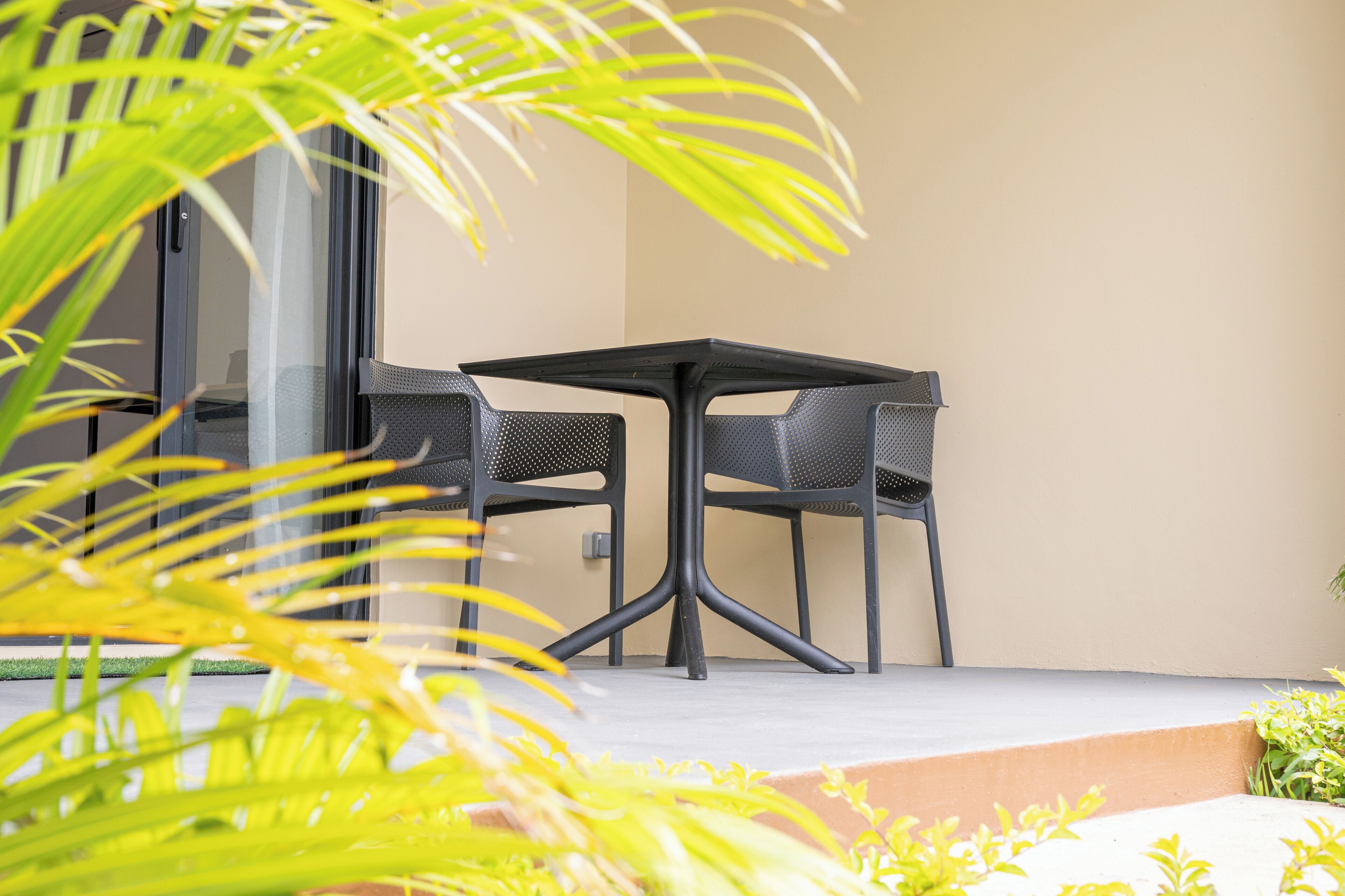 An outdoor seating area with a table and chairs, surrounded by greenery.