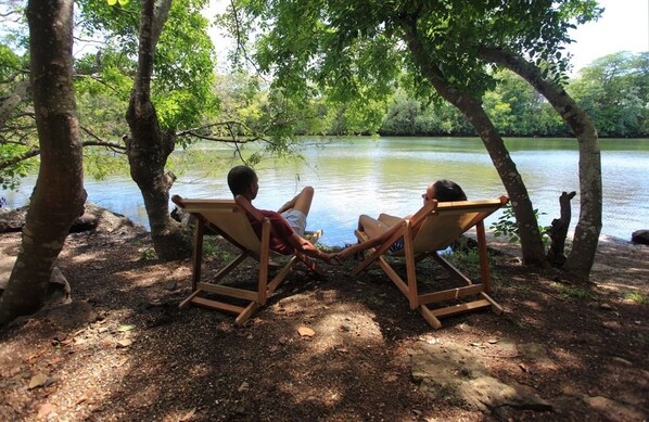 Two people sitting on wooden chairs facing a body of water, surrounded by trees. - EvaZion (Grand River South East)