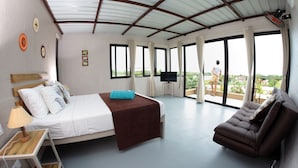 A bedroom with a bed, a sofa, a TV, and large windows.