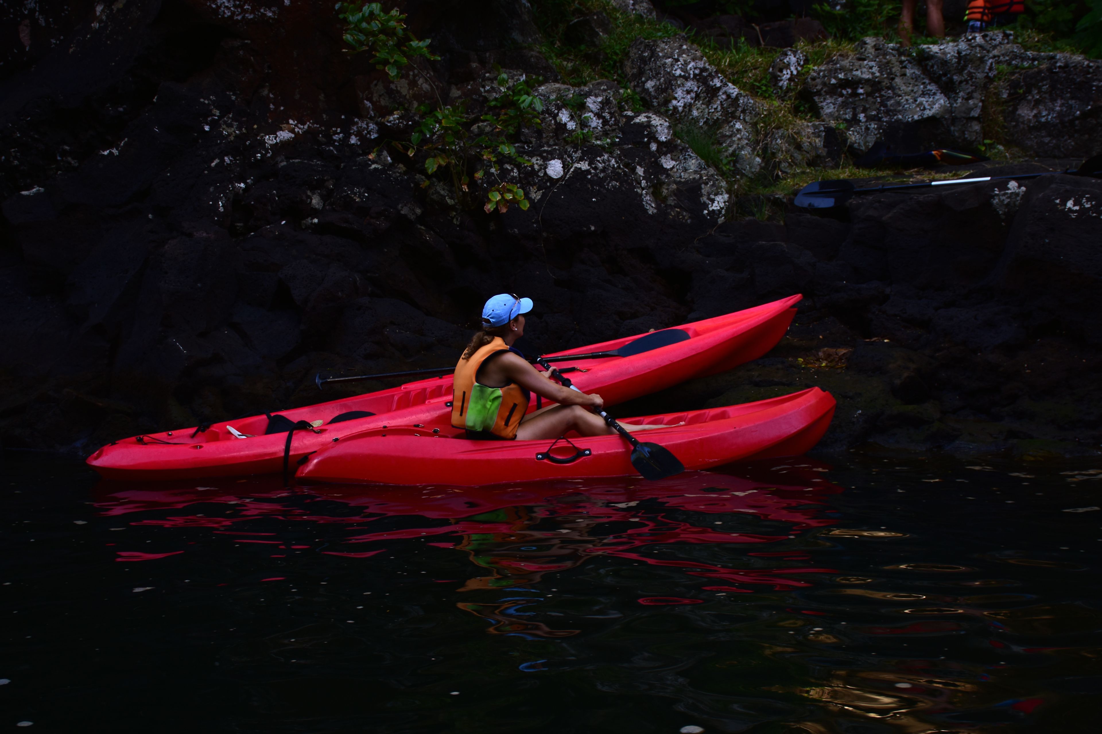 A person sitting on a red kayak in calm water.