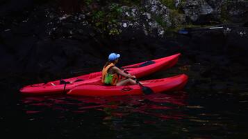 A person sitting on a red kayak in calm water.