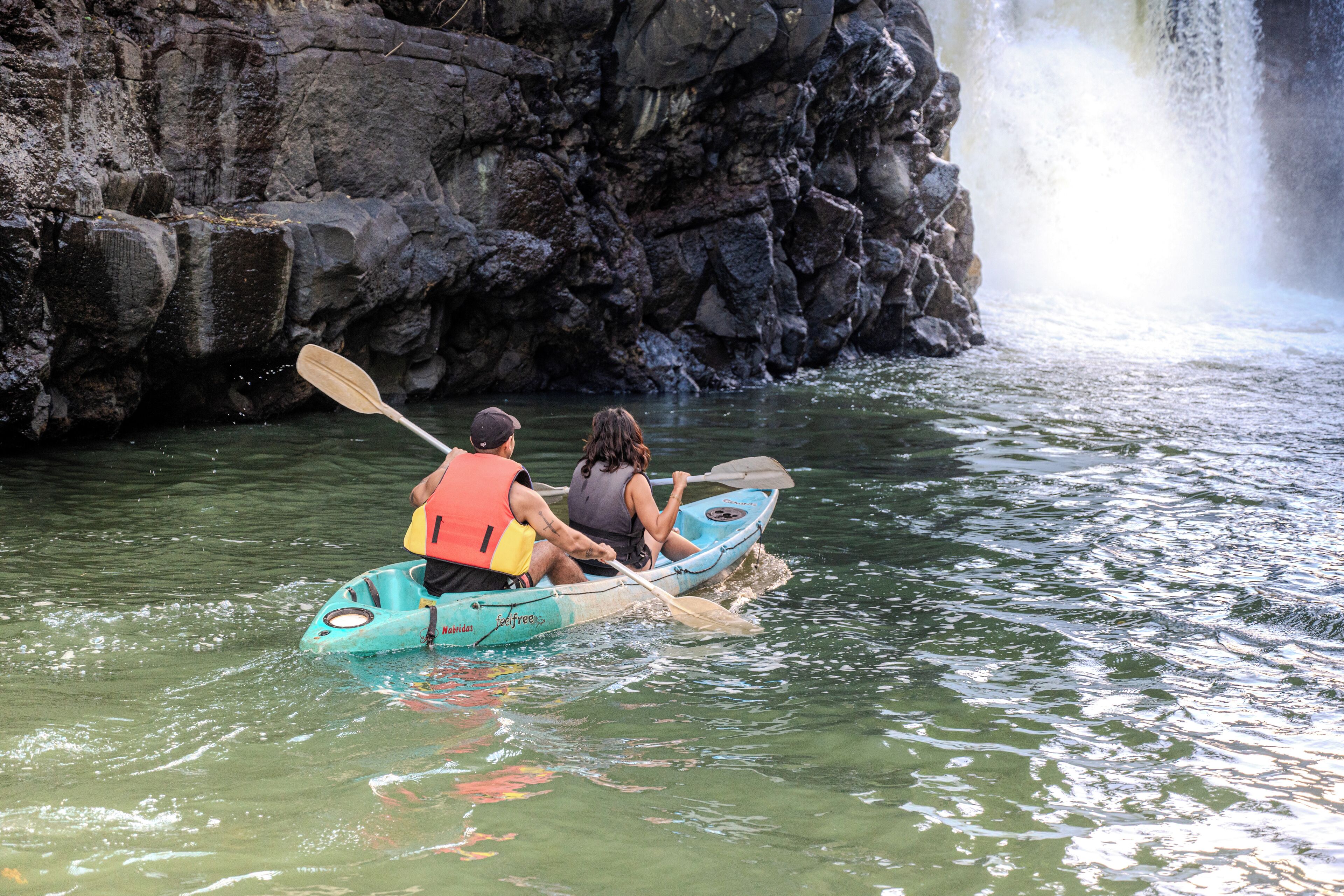 A couple in a kayak on a river with a waterfall in the background.