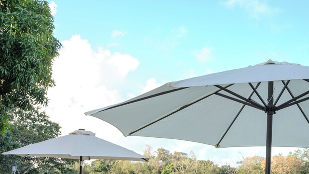 A wooden deck with outdoor furniture, including a round table and chairs, and two large umbrellas providing shade.