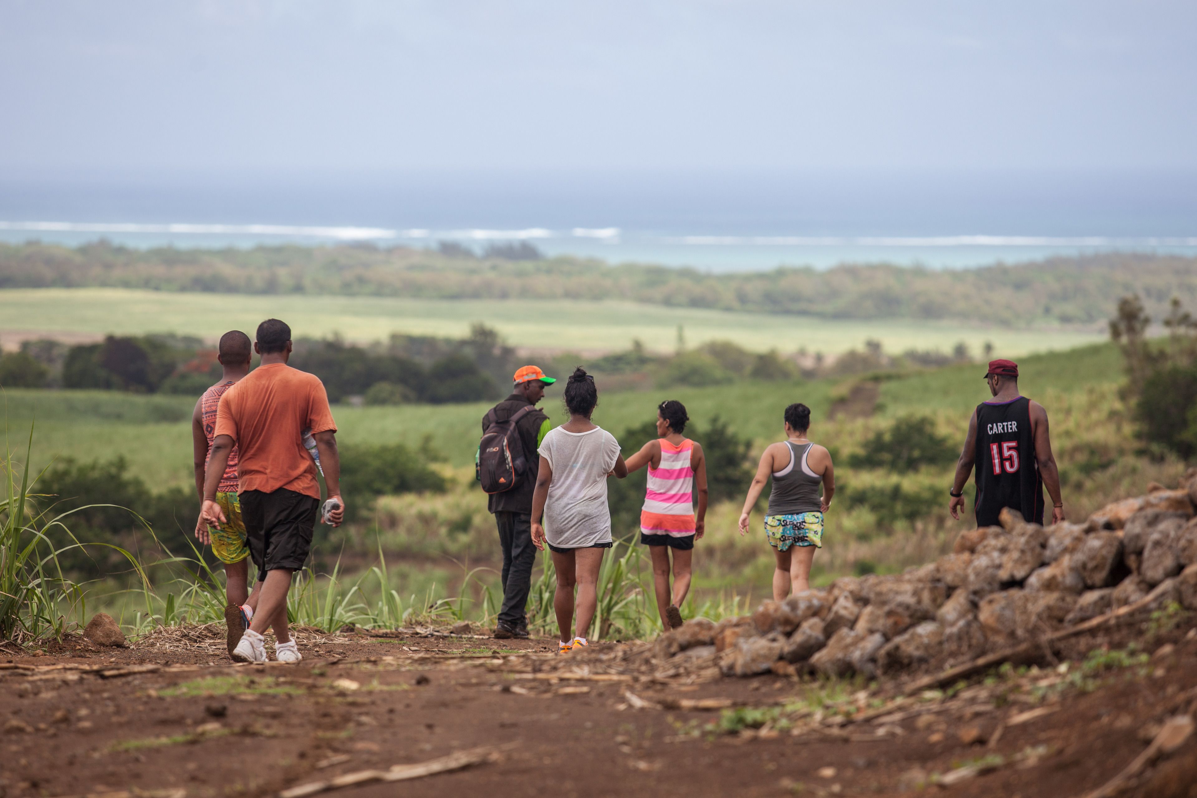 A group of people walking on a dirt path with a view of a green landscape and water in the distance.