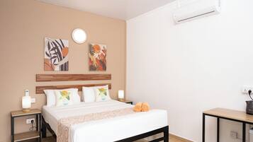 Habitación de hotel con cama, mesitas de noche, decoración en la pared, unidad de aire acondicionado y toma de corriente.