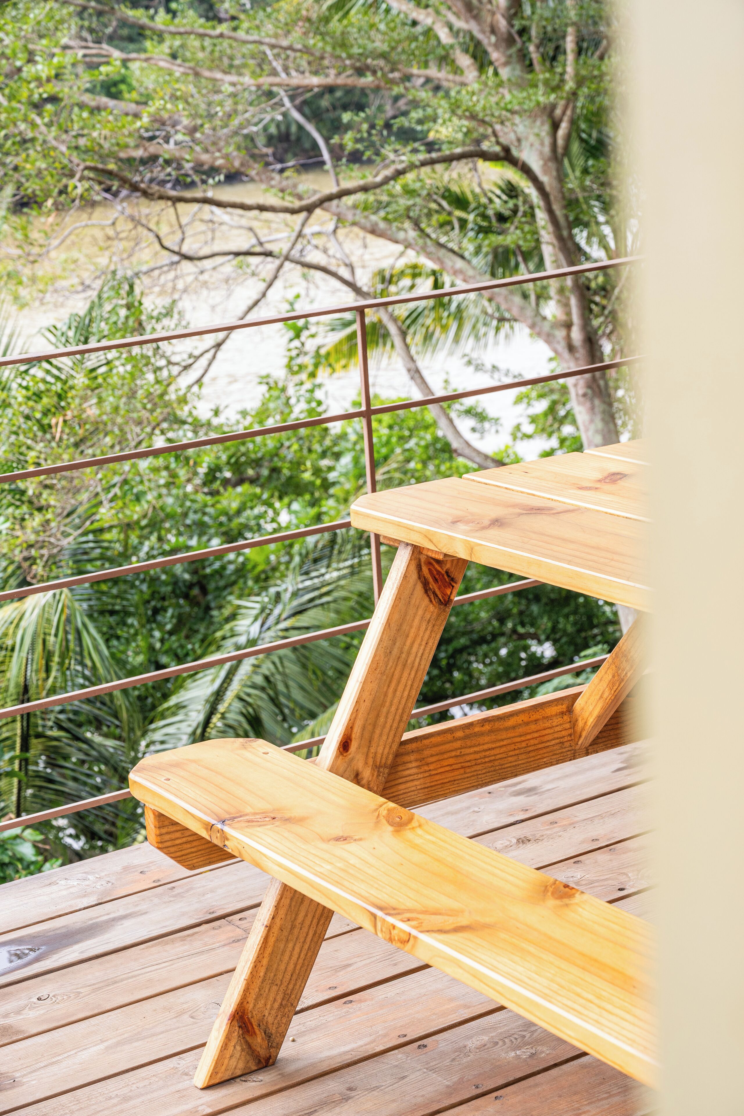 A wooden deck with a table and bench, overlooking a beach and greenery.