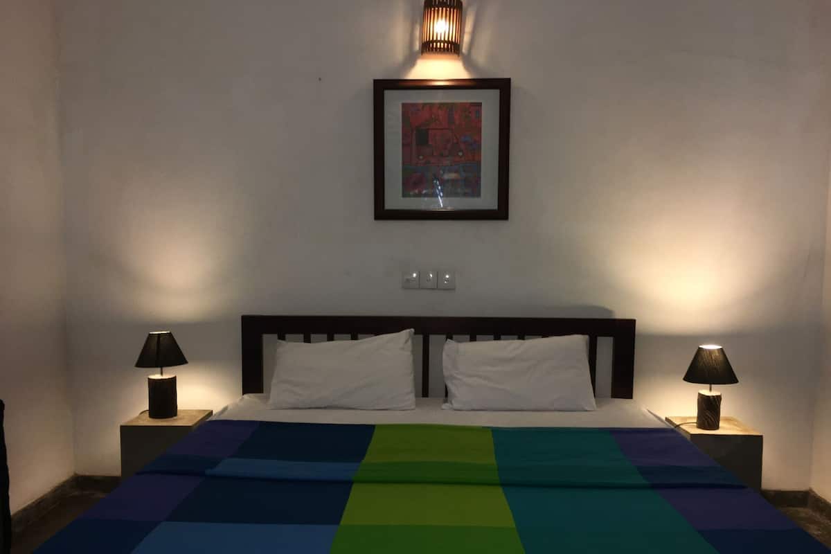 Un dormitorio con una cama, dos lámparas de noche, un cuadro enmarcado en la pared y un enchufe sobre la cama.
