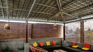 An outdoor seating area with a concrete floor, cushioned seating, and hanging pendant lights. - Colombo Beach Hostel (Mount Lavinia)