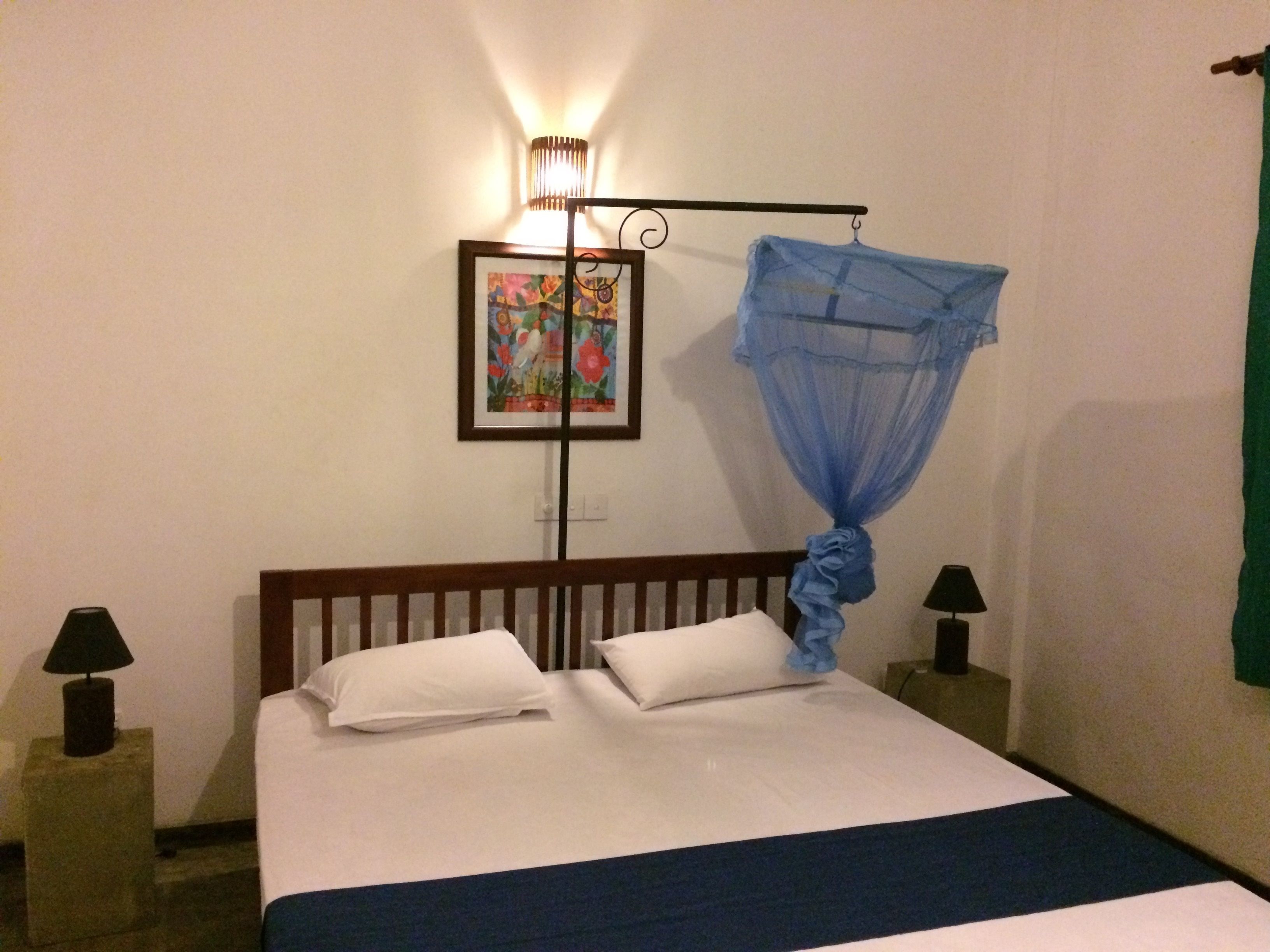 A hotel room with a bed, two bedside lamps, a wall-mounted picture, and a mosquito net.