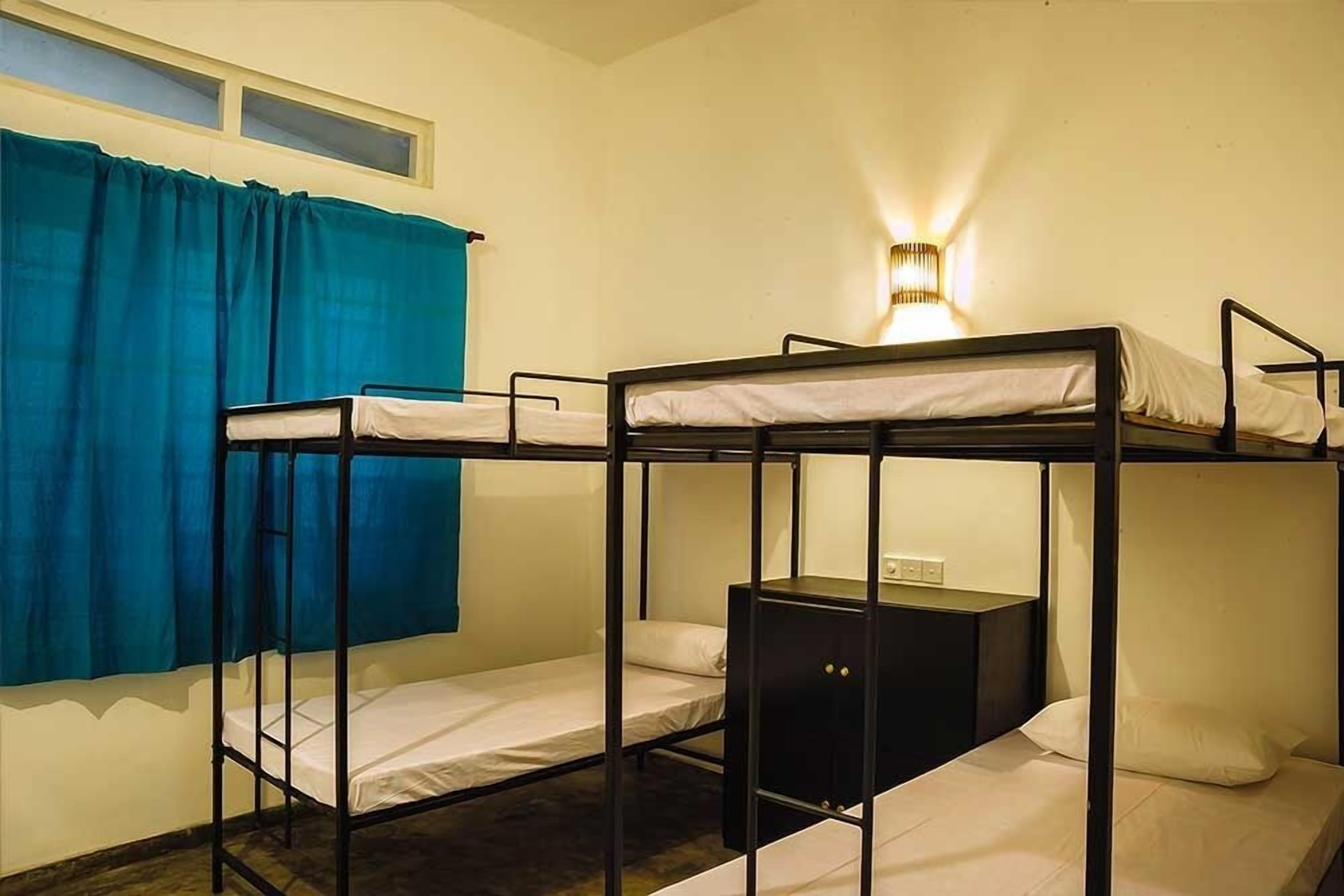 Quarto com beliche, janela, cortinas e luminária fixada na parede.