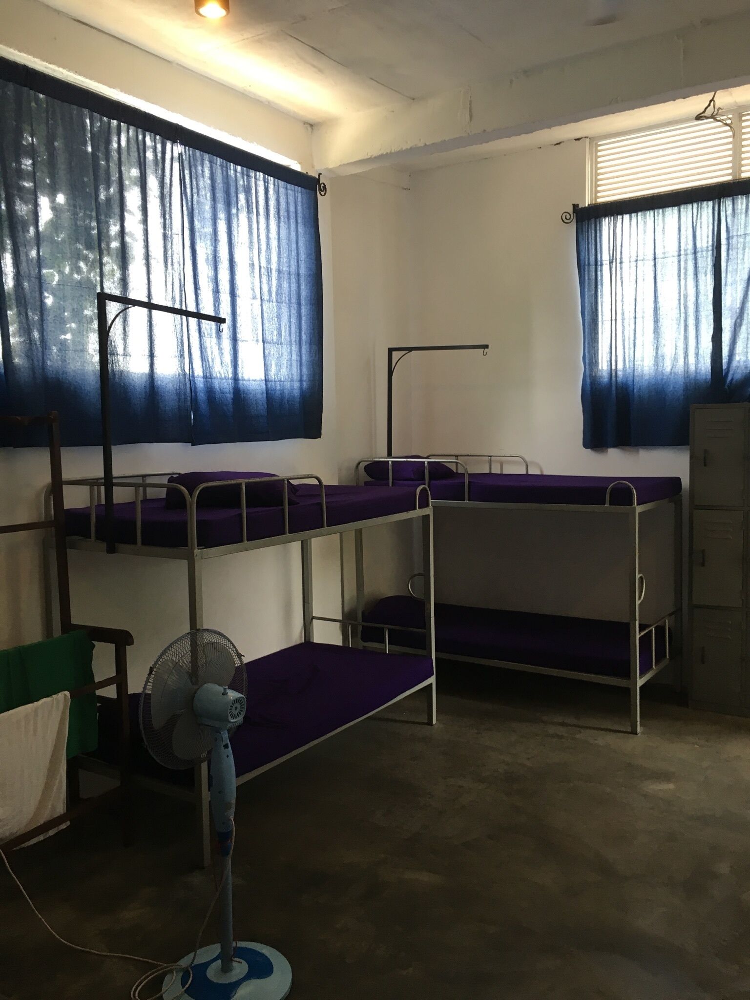 Un dormitorio con literas, un ventilador de pie y una ventana con cortinas.