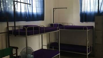 Un dormitorio con literas, un ventilador de pie y una ventana con cortinas.