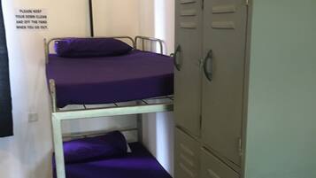 A bunk bed with purple bedding and a metal frame, a green metal locker, and a sign on the wall.