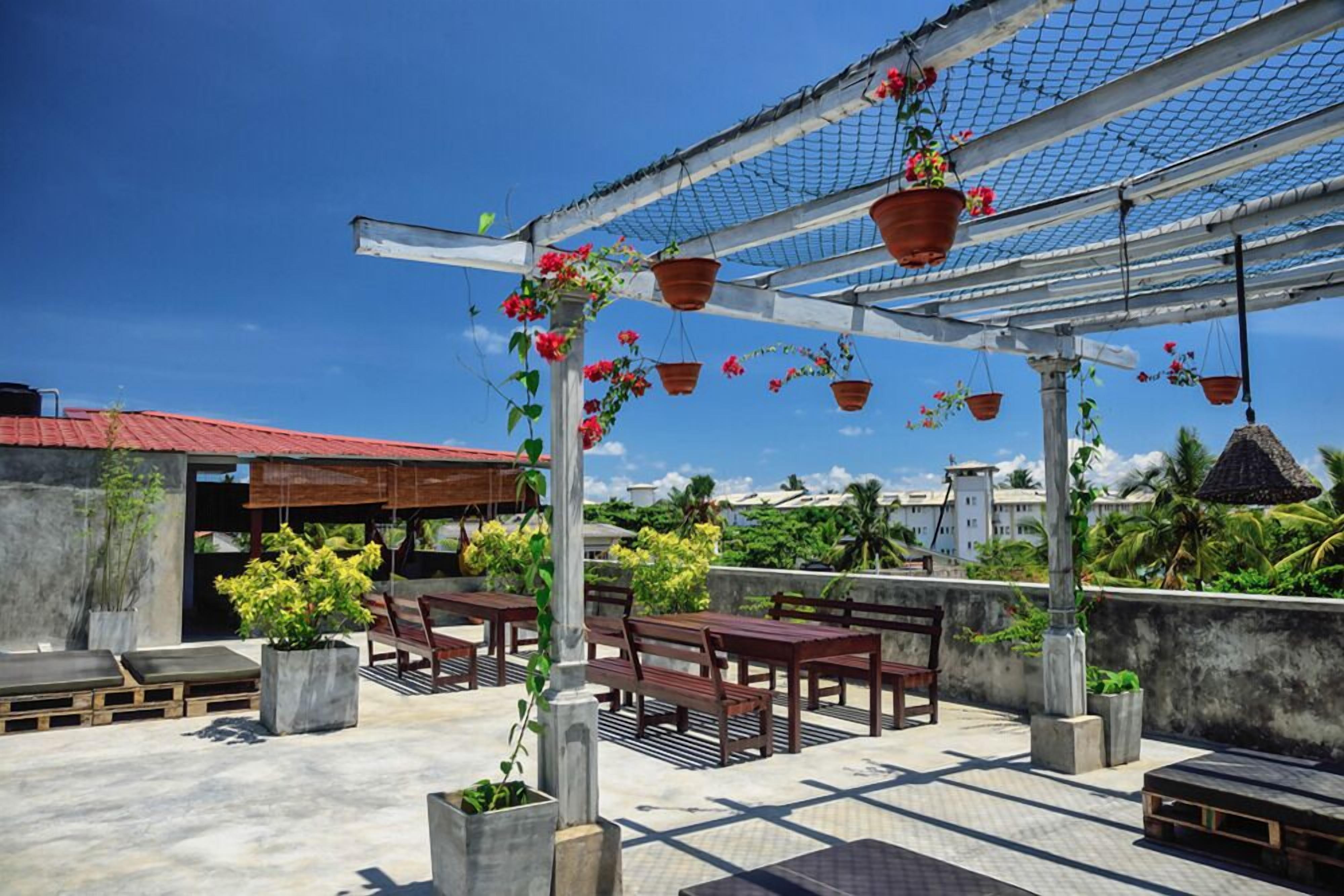 Una terraza en la azotea con bancos de madera, plantas en macetas y cestas de flores colgantes.