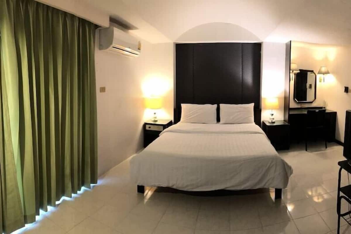 A hotel room with a bed, a TV, a desk, a chair, a mirror, and a window with curtains.