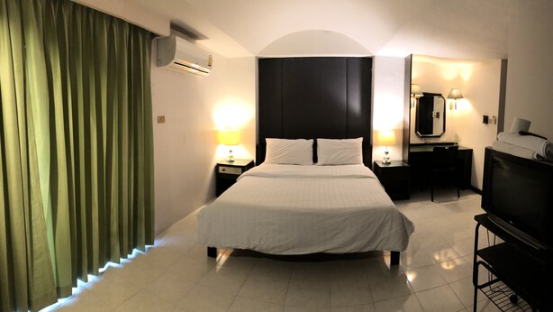 A hotel room with a bed, bedside lamps, a TV on a stand, a desk, a chair, a mirror, and a curtain. - S.C. Heritage Hotel (Hat Yai)