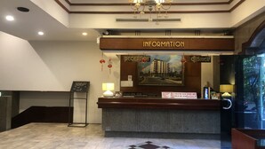 A hotel reception area with a reception desk, a chandelier, a framed cityscape picture, and a check-in counter. - S.C. Heritage Hotel (Hat Yai)