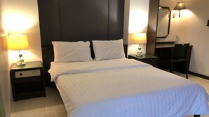 A neatly made bed with white linens, two bedside tables with lamps, a chair, and a large mirror on the wall. - S.C. Heritage Hotel (Hat Yai)