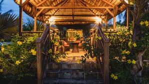 A wooden gazebo with a thatched roof, surrounded by lush greenery and yellow flowers. - Ocean Beach Villa (Trou aux Biches)