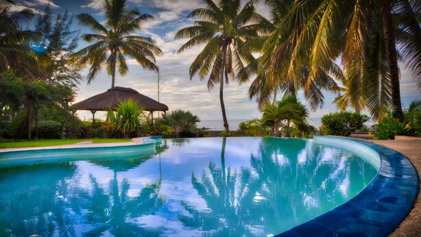 A swimming pool surrounded by palm trees and a thatched-roof structure. - Ocean Beach Villa (Trou aux Biches)