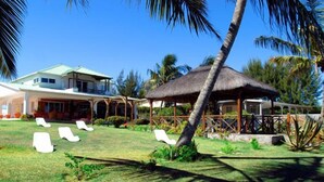 A resort with a house, a thatched-roof structure, and several white lounge chairs on a grassy lawn. - Ocean Beach Villa (Trou aux Biches)