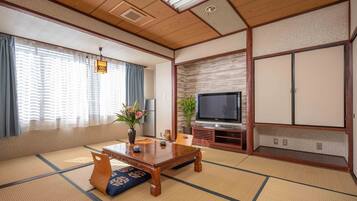 Une pièce de style japonais traditionnel, avec un sol recouvert de tatamis, une basse table en bois, un téléviseur et des portes coulissantes.
