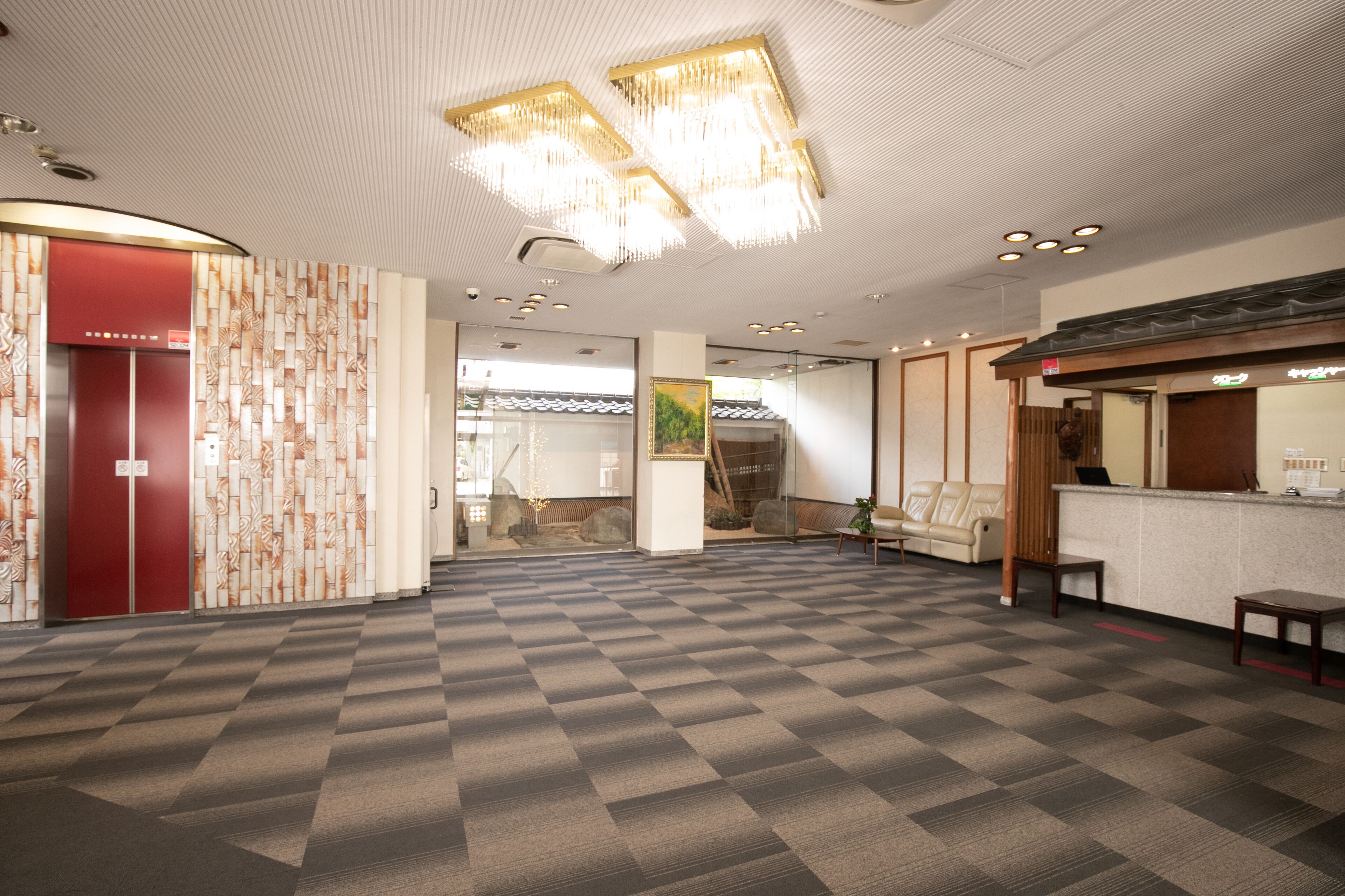 A spacious lobby with a checkered floor, a reception desk, and a red elevator.