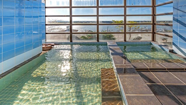 A clear indoor swimming pool with a view of the sea through large windows. - New Makomo Hotel (Itako)