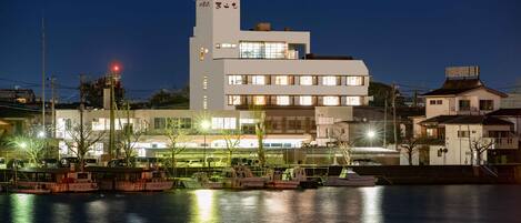 Ein mehrstöckiges Gebäude am Wasser mit einem markanten Turm und einem Steg mit Booten.
