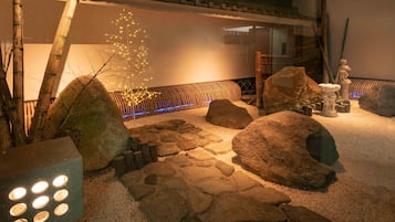 Een traditionele Japanse tuin met stenen paden, grote rotsen, een bamboeboom en een standbeeld.