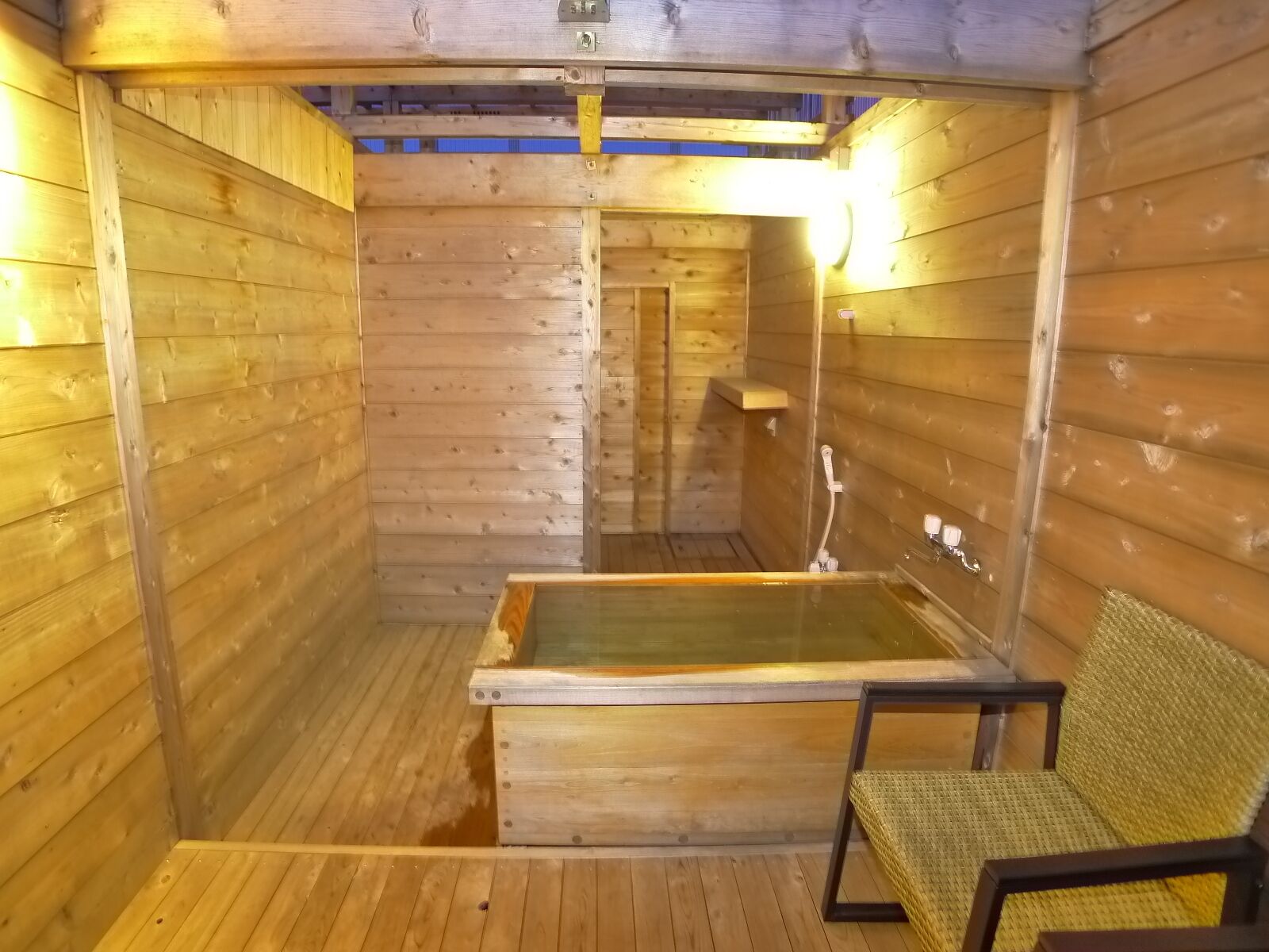 A wooden sauna with a glass-enclosed hot tub, a wooden bench, and a wall-mounted showerhead.
