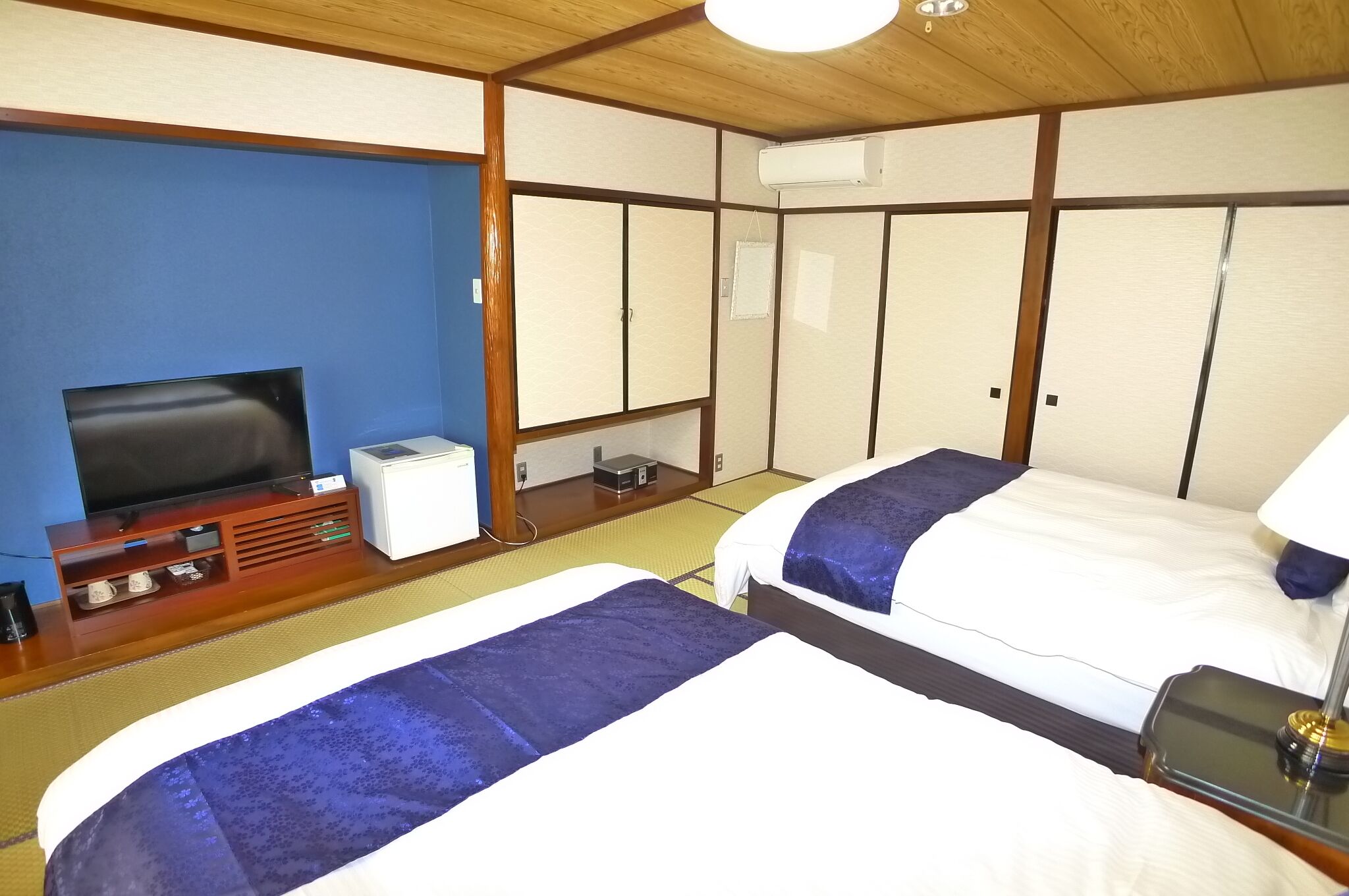 A hotel room with two beds, a TV, a small desk, and a storage unit.