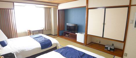 A hotel room with two beds, a television, a small desk, and a window with curtains.