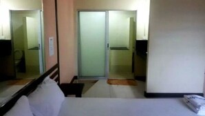 A hotel room with a bed, a mirror, a sliding door to the bathroom, and a small rug on the floor. - PR Resort Hat Yai (Hat Yai)